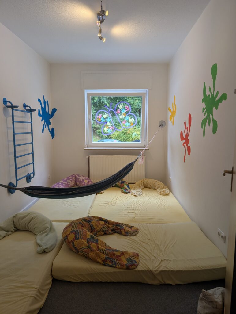 Gemütlicher Ruhe- und Bewegungsraum in der Kindertagespflege mit großem Matratzenlager, Hängematte und einer Sprossenwand an der Wand.
