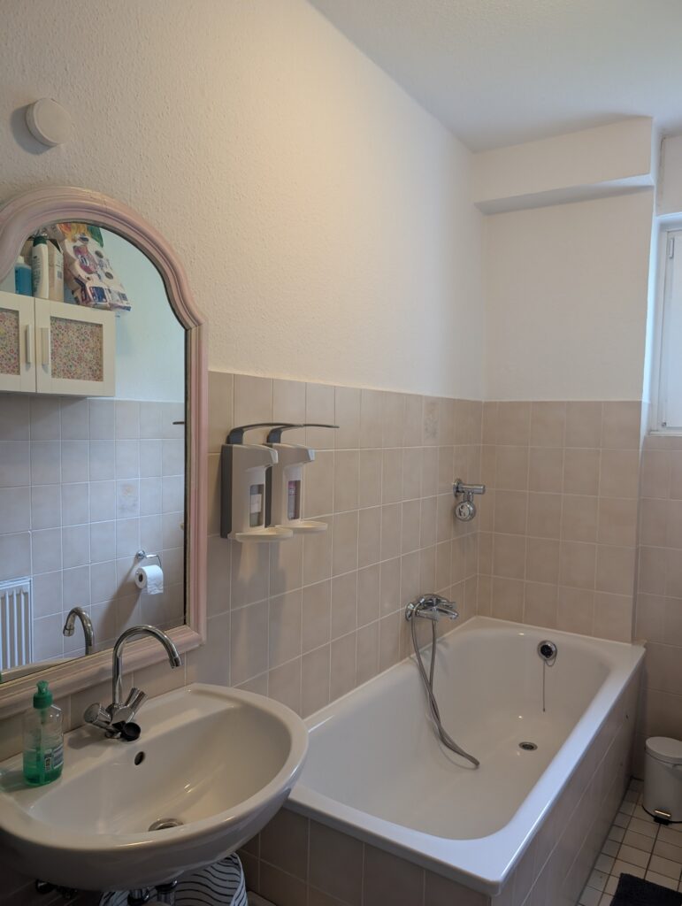 Heller Waschbereich im Badezimmer der Kindertagespflege mit Waschbecken, großem Spiegel und Badewanne für die tägliche Hygiene.