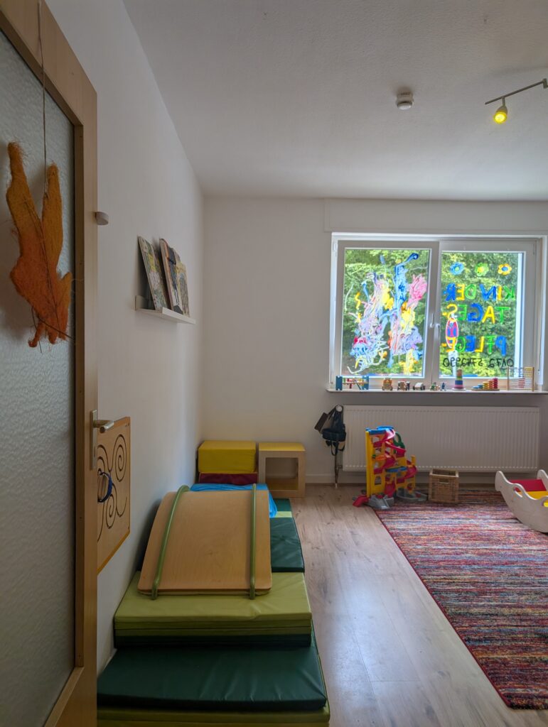 Heller Bewegungsraum in der Kindertagespflege mit weichen Matten, Holzrutsche und Kugelbahn zur Motorikförderung.