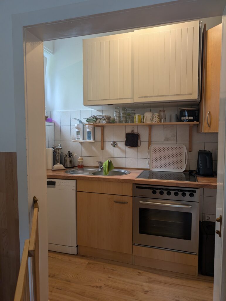 Helle Küche in der Kindertagespflege mit moderner Ausstattung und Sicherheitsgitter für die Zubereitung frischer Mahlzeiten.