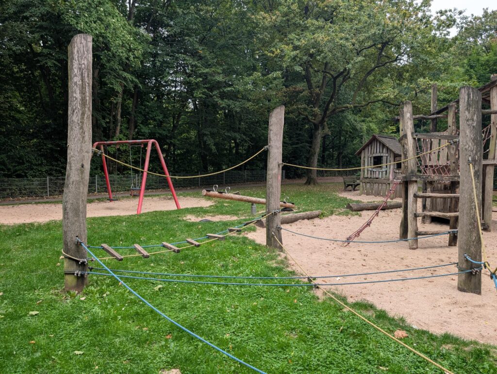 Großzügiger Spielplatz im Grünen direkt vor der Tür mit Klettergerüst aus Holz, Schaukel und Sandkasten für Ausflüge und Bewegung an der frischen Luft.